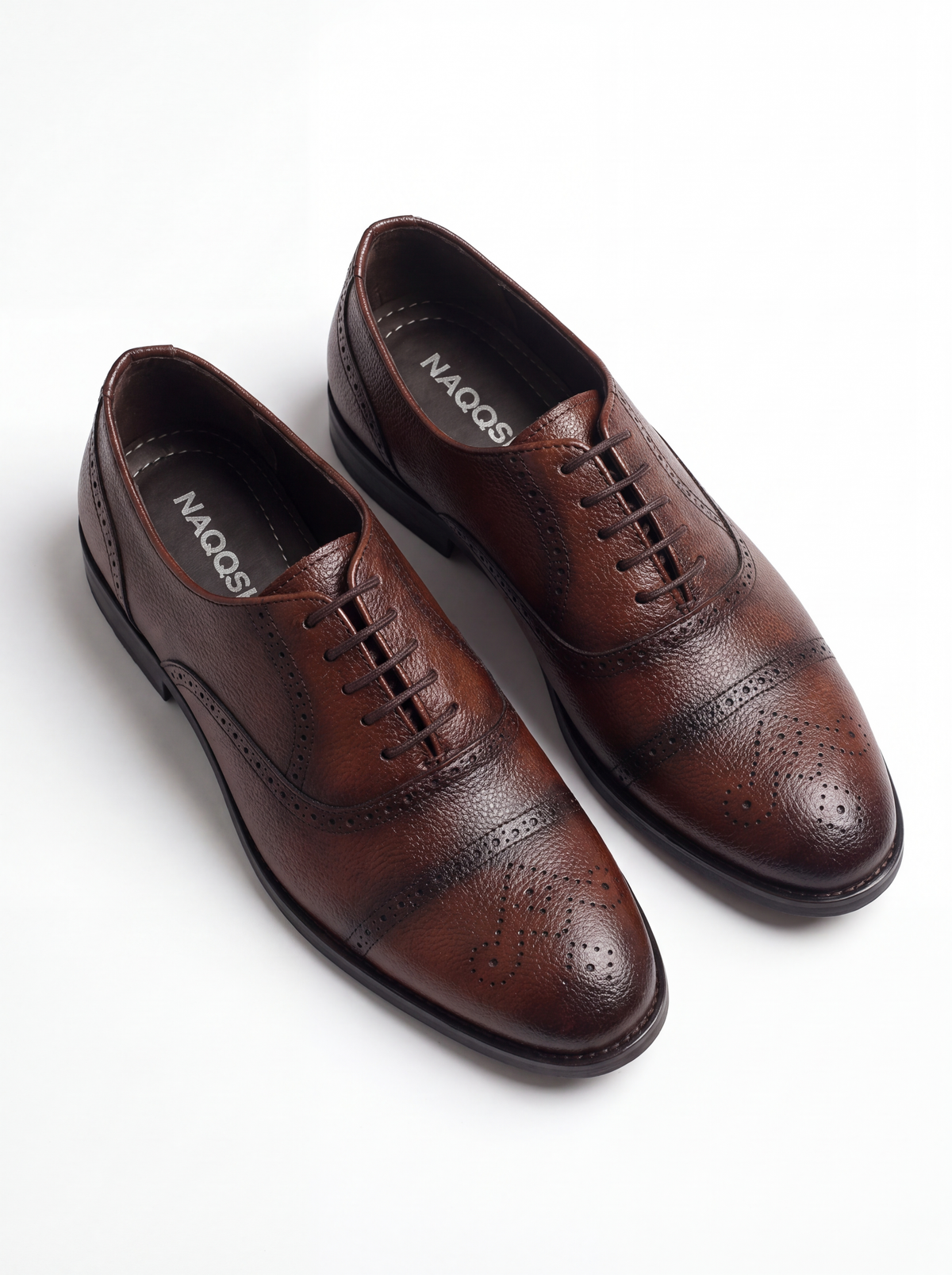 A pair of brown wingtip oxford shoes with brogue detailing, displayed on a clean white background. 