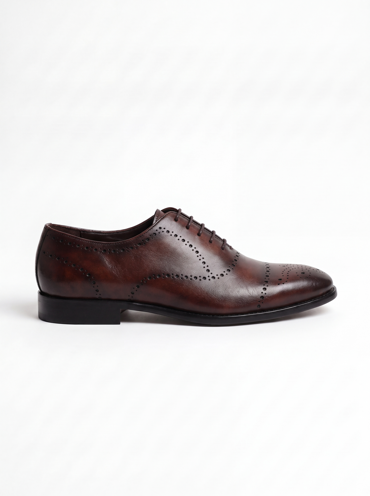 A single dark brown oxford wingtip shoe with decorative brogue perforations, shown in a side profile against a clean white background.